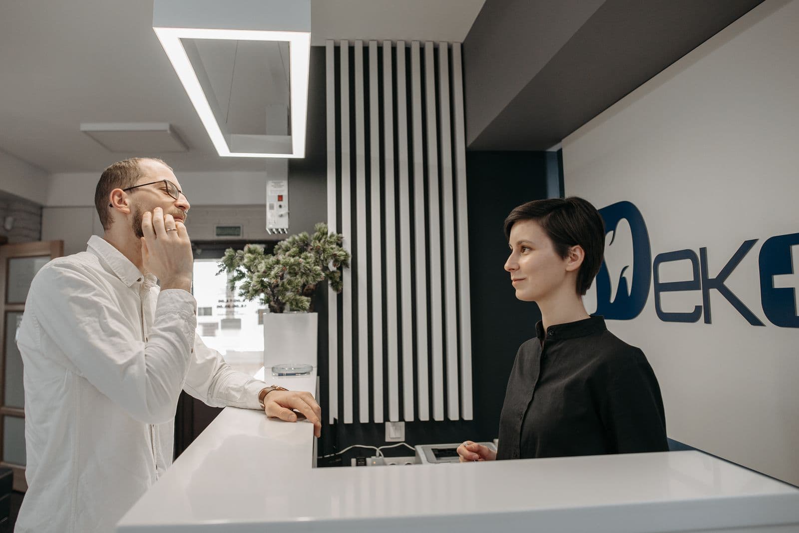 A patient talks with a receptionist at a dental clinic front desk.