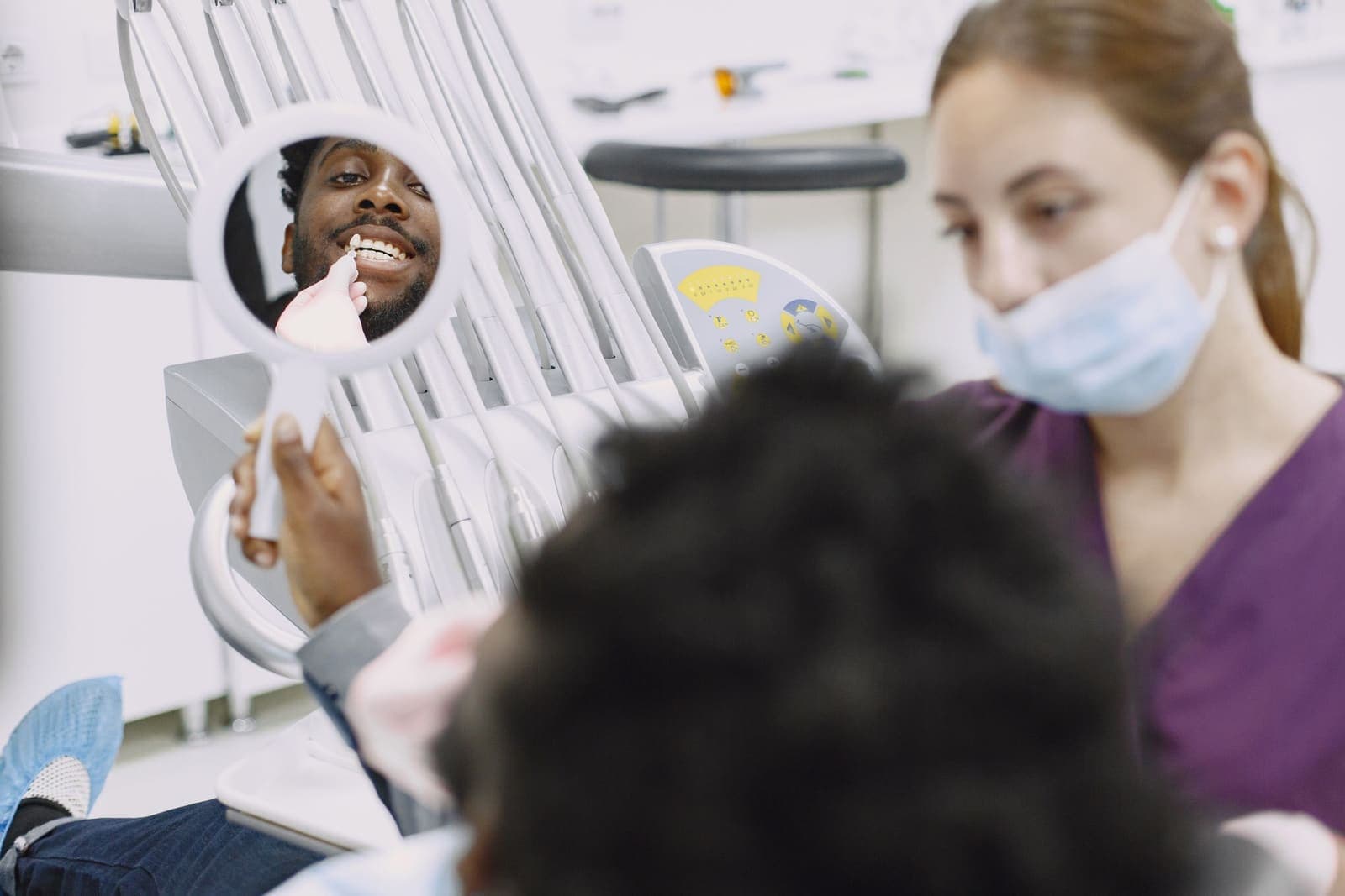 A dentist examines a patient's anterior teeth with a mouth mirror during a chairside check.