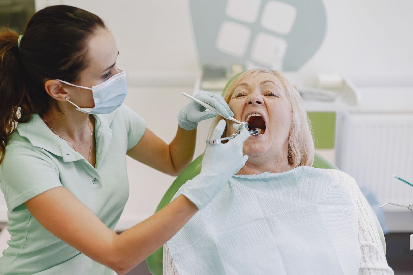 A female dentist examines a senior woman patient during a dental appointment.